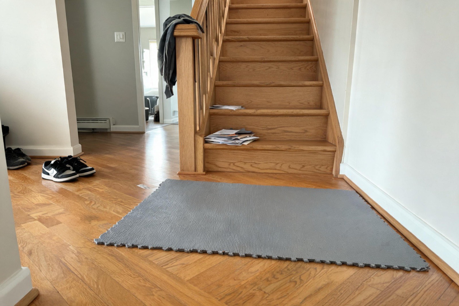 A gray yoga mat cut to size and laid at the base of a wooden staircase.