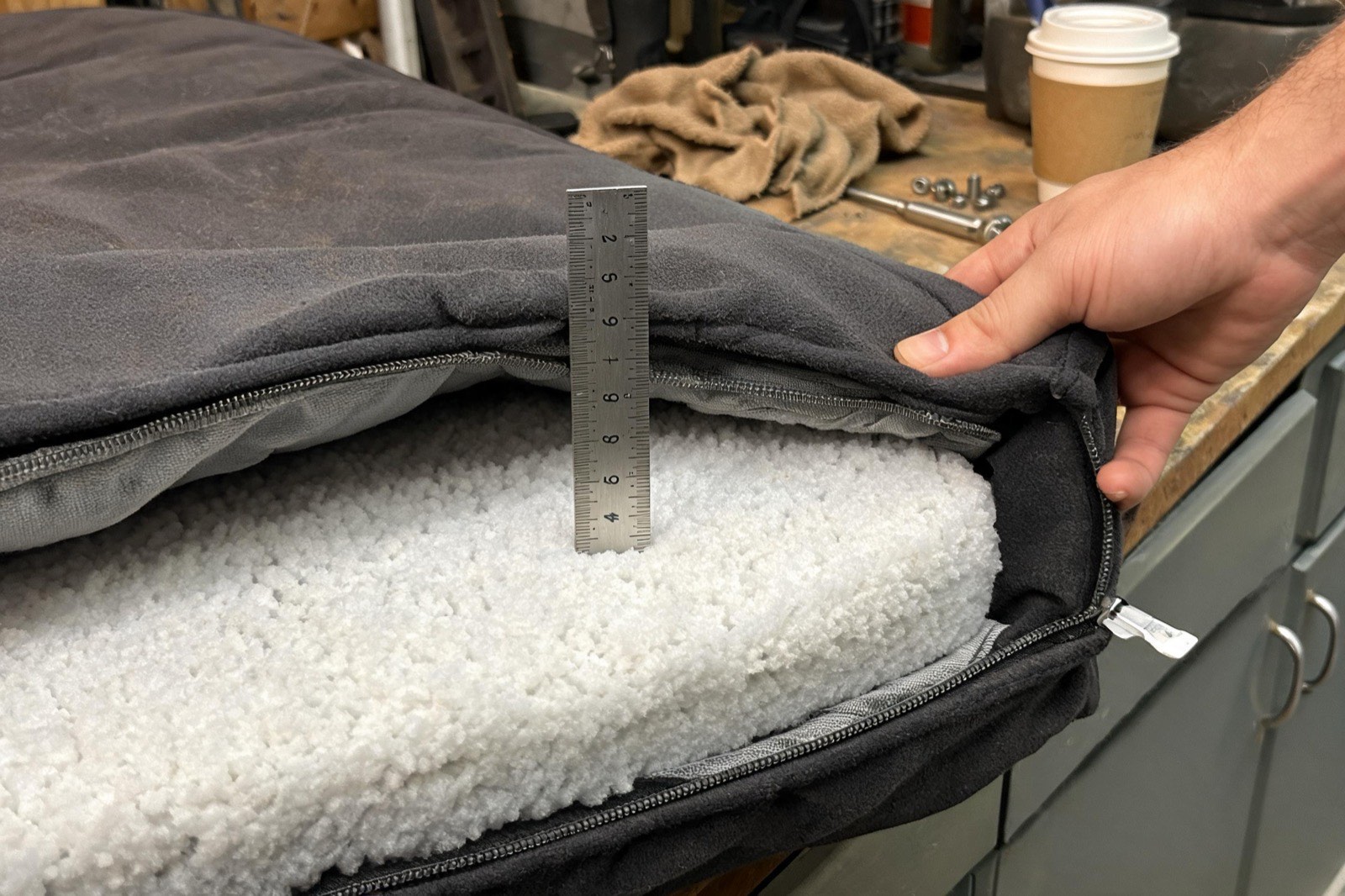 A steel ruler pushed into the open corner of a thick foam dog bed, reading just under seven inches.